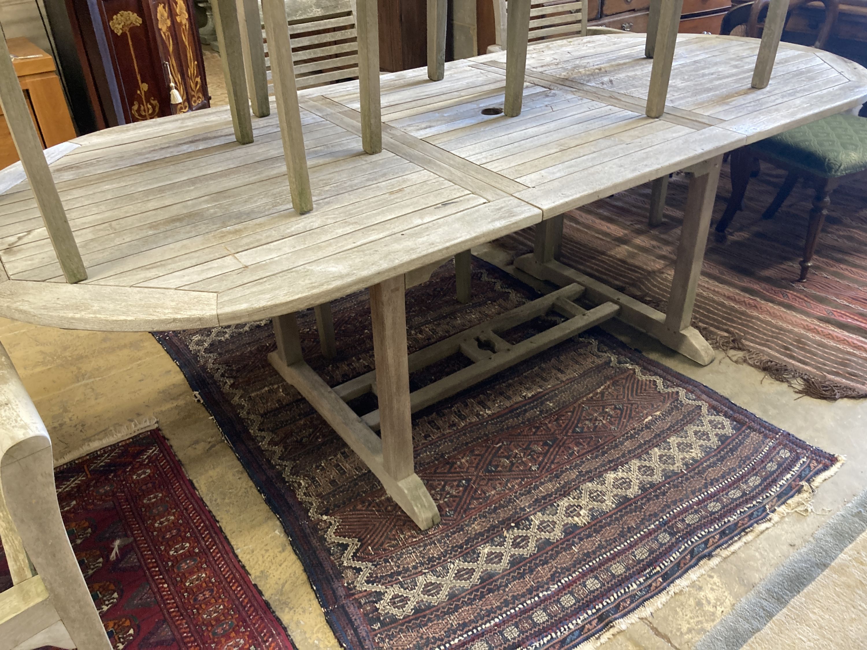 A weathered teak extending garden table, length 240cm extended, depth 100cm, height 77cm together with a set of seven weathered teak elbow chairs
